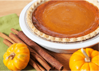 A pumpkin pie with cinnamon sticks and small pumpkins on the side.