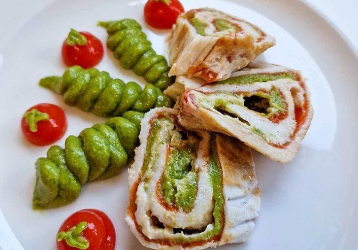 Chicken roll-ups with avocado and cherry tomatoes on a white plate.
