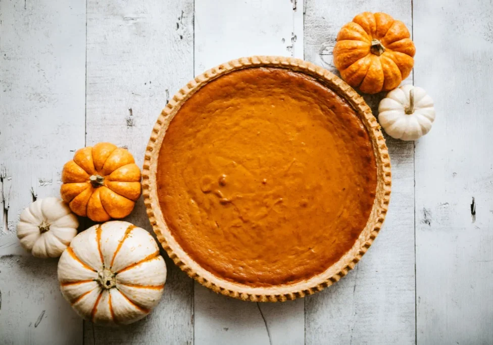 A classic pumpkin pie surrounded by small decorative pumpkins.
