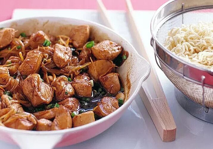 Bowl of cooked chicken pieces with sauce and herbs.