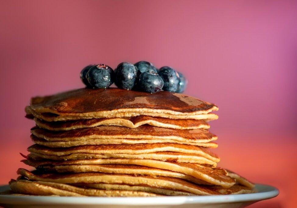 Stack of pancakes topped with fresh blueberries on a plate.